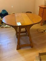 Round wooden table with drop sides, shown from an angle, on a wooden floor.