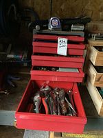 Red metal tool chest with many drawers, top drawer open showing assorted wrenches and pliers with red and black handles.