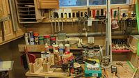 Wide view of workbench showing assorted containers with liquids, wooden tool organizers, screwdrivers, and hardware items.