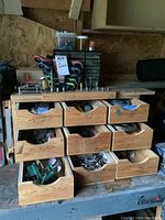 Full view of wooden drawer unit showing nine drawers partially open revealing various tools and hardware inside, with small hardware cabinet on top containing screws and bolts.