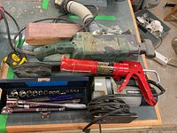 Overview of all tools including jigsaw, caulking gun, socket set, tape measure, and sander on table.