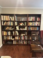 Front view of three tall dark wood book shelves filled with books to demonstrate size and use.