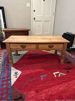 Front view of the antique wooden coffee table showing two drawers with decorative handles and turned legs, placed on a colorful rug in a room.