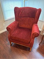 Front view of red velvet wingback armchair showing seat cushion, armrests and wooden legs.