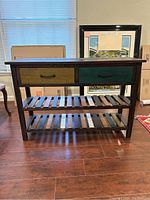 Front view of wooden sideboard showing two drawers with different accent colors (yellow and green) and two slatted shelves below.