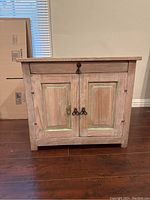 Front view of the cabinet showing distressed wood, white stain, teal highlights on the door panels, metal handles, and keyhole.