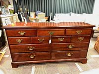 Front view of a dark brown wooden dresser with nine drawers and brass-colored metal hardware pulls.