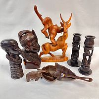 Photo showing a collection of ethnographic carved wooden sculptures including human busts, animal figures, two candlestick holders, and a wooden serving spoon with beadwork.