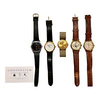 Five wristwatches laid flat and side by side showing variety in band materials (black leather, brown leather, gold metal) and face colors (dark, light, gold). Also visible is a card with 'CONSORTIUM' branding.