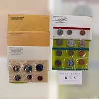 Photo of four vintage US Treasury Department coin sets sealed in plastic packaging along with official envelopes from US Mint offices.