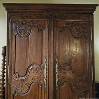 Full front view of large wood wardrobe with detailed carvings and brass handles on double doors