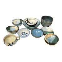 Top view of various pottery bowls and one cup arranged together showing mix of blues, greens, and natural tones with different shapes and textures.