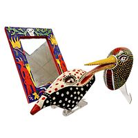 Photo showing a carved and painted mirror with a colorful border, alongside two decorative masks with elongated beak-like snouts and intricate painted designs.