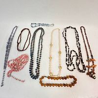 Seven assorted beaded necklaces displayed flat on white background showing variety in color, bead size and material.