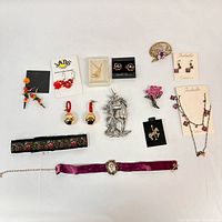 Top-down view of assorted small accessories including earrings, brooches, choker bracelet, and a necklace set arranged on white background.