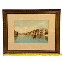 Framed watercolor painting showing Venice canal scene with gondolas, matted with cream-colored matte, brown wooden frame. Signed bottom left, width approx. 30 inches.