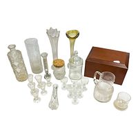 Overall group photo showing various clear glass vases, vessels, numerous small clear shot glasses, two glass jars (one with cork lid, one with glass lid), a small pitcher, a short tumbler, a textured and a flared vase, and a wooden box with a chip on top.