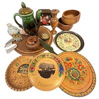Photo showing a collection of vintage wooden bowls, decorative wooden plates with hand-painted floral and place designs including one labeled Lausanne, a green ceramic spouted pot, wooden candlestick, and small wooden containers and boxes.