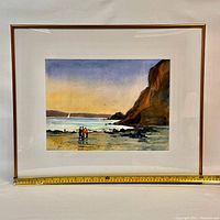 Framed watercolor painting showing beach scene with cliffs and figures, capturing color and composition.