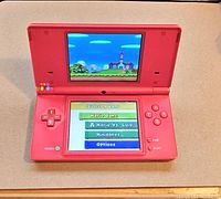 Red Nintendo DS powered on, displaying game menu with Mario game options.