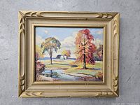Full front view of framed landscape painting featuring autumn trees, house, and water body