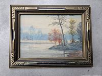 Full view of the framed landscape painting showing a lakeside scene with trees and cabins.