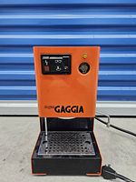 Front view of orange/red Gaggia espresso machine showing control panel, drip tray, steam wand.