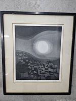 Full view of framed lithograph artwork showing black and white abstract landscape with geometric buildings and large bright circular light source