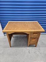 Front angled view showing desk top and drawers with wood grain detail and solid construction