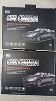 Closed boxes of 2 generic HD car cameras with sports car image on packaging