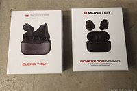 Photo of the product boxes for Monster Clear Talk and Monster Achieve 300 Airlinks earbuds, showing branding and product images on the front.