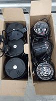 6 party lights packed in 2 cardboard boxes - 3 black circular base lights on the left and 3 clear dome-shaped disco lights on the right, all with power cords and plugs.