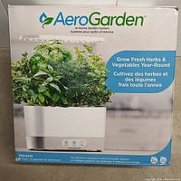 Front of box showing AeroGarden logo, in-home garden system, image of the unit growing herbs, and branding for year-round fresh herbs and vegetables with 6 seed pods included.