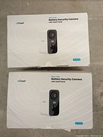 Two ioGeek battery security camera boxes, each labeled wire-free with solar panel. White with black front face cameras pictured on boxes.