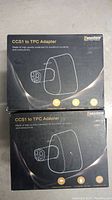 Two boxed Hanshow CCS1 to TPC Adapter packages with printed graphics and branding on the boxes.