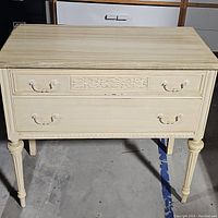 Front view of cream table showing two drawers and carved detail on the top drawer