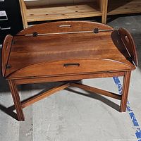 Front view showing wooden butler's tray table with sides folded up, integrated cutout handles visible.