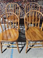 Set of four antique wooden chairs with spindle backs arranged closely together showing top and front views.
