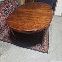 Full view of antique six-seater wooden dining table on patterned carpet with rounded edges and warm wood tone.