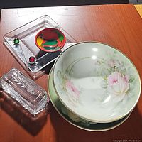 Collection of serving dishes including floral bowl with matching plate, clear glass butter dish, and decorative small glass plate on acrylic base.