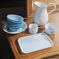 Overview of all items in the lot including six blue bowls stacked on a floral white plate, white pitcher, rectangular tray, and three small round/oval bowls or containers.