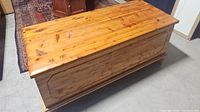 Photo of large cedar chest showing top and decorative front panel, wood grain and finish.