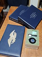 Three navy blue coin albums on wooden table with green felt-lined cleaning kit box