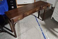 Wooden console desk showing full front view with three drawers and brass handles, standing on four straight legs.