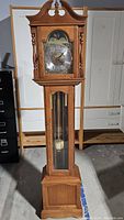 Full front view of the grandfather clock showing the entire wooden case, pendulum visible through glass door.