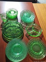 Top view showing assortment of green depression glass items including plates, divided bowl, cups and serving trays arranged on wooden surfaces.