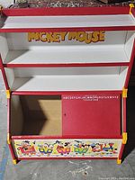 Full front view of the multi-tier toy shelf with Mickey Mouse branding on the second shelf and colorful Disney character train design on lower storage compartment.