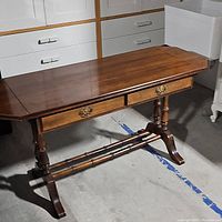 Full view of cherry wood drop leaf table showing top, drawers, turned legs, and stretcher base.