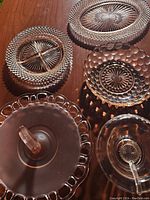Five pink Depression glass serving dishes featuring various patterns including quilted, starburst, and hobnail motifs. Includes covered dish, oval platters, divided plate, and round bowl.