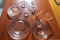 Tabletop display of pink Depression glass plates, candlesticks and vases showing details of texture, ribbing, and shape.
